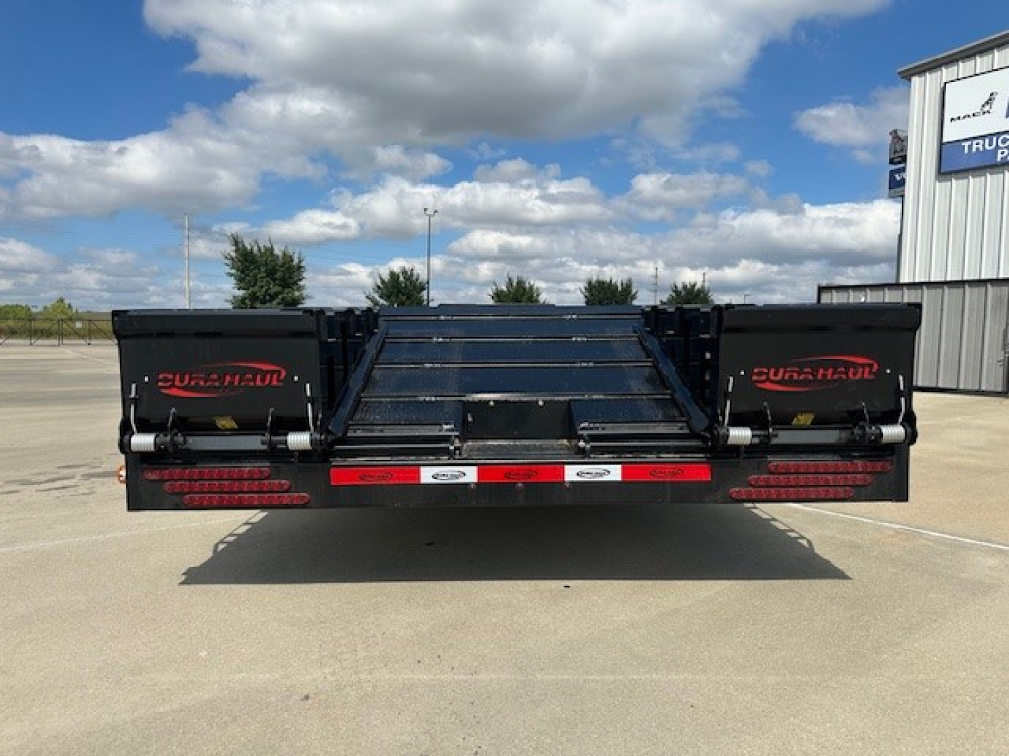 Back view of a new 53' drop deck trailer with spread tail ramps, Dura Haul branding visible on both sides, black metal, with red and white rear lights.