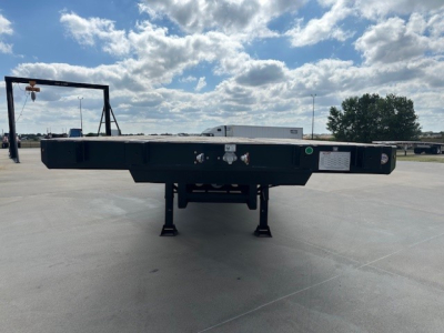 Trailer rear view showing drop deck trailer with spread axle, low landing gear and ramps folded under deck