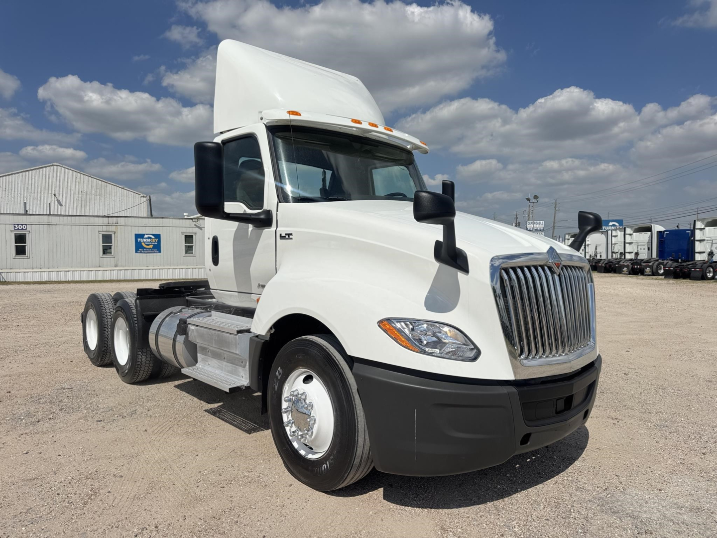 International LT conventional daycab truck showing white cab, large chrome grille, black bumper, dual rear axles, and daylight.