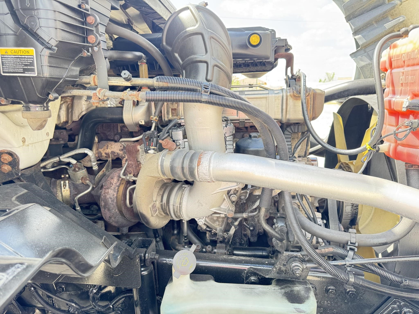 Truck engine bay showing labeled components and hoses; visible text includes caution sticker and various hoses and turbo lines.