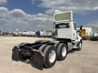 Semi truck chassis with dual rear axles and fifth wheel, 2019 International LT semi tractor, white cab, exposed engine bay fold-down hood, parked in gravel lot.