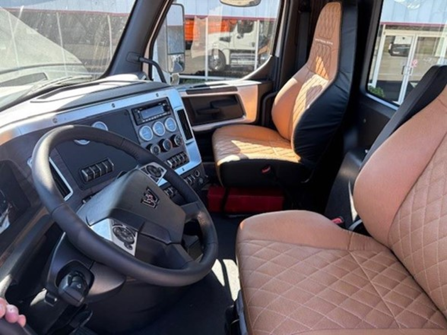 Cab interior of a 2026 Western Star 49X Day Cab showing steering wheel, dashboard with gauges, and tan quilted seat upholstery.
