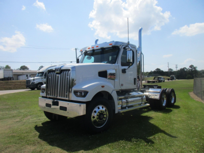 Western Star 49X day cab tractor in white, front grille with vertical bars, dual rear axles, chrome fuel tanks, and tall exhaust stack; open cab windows, clear sky.