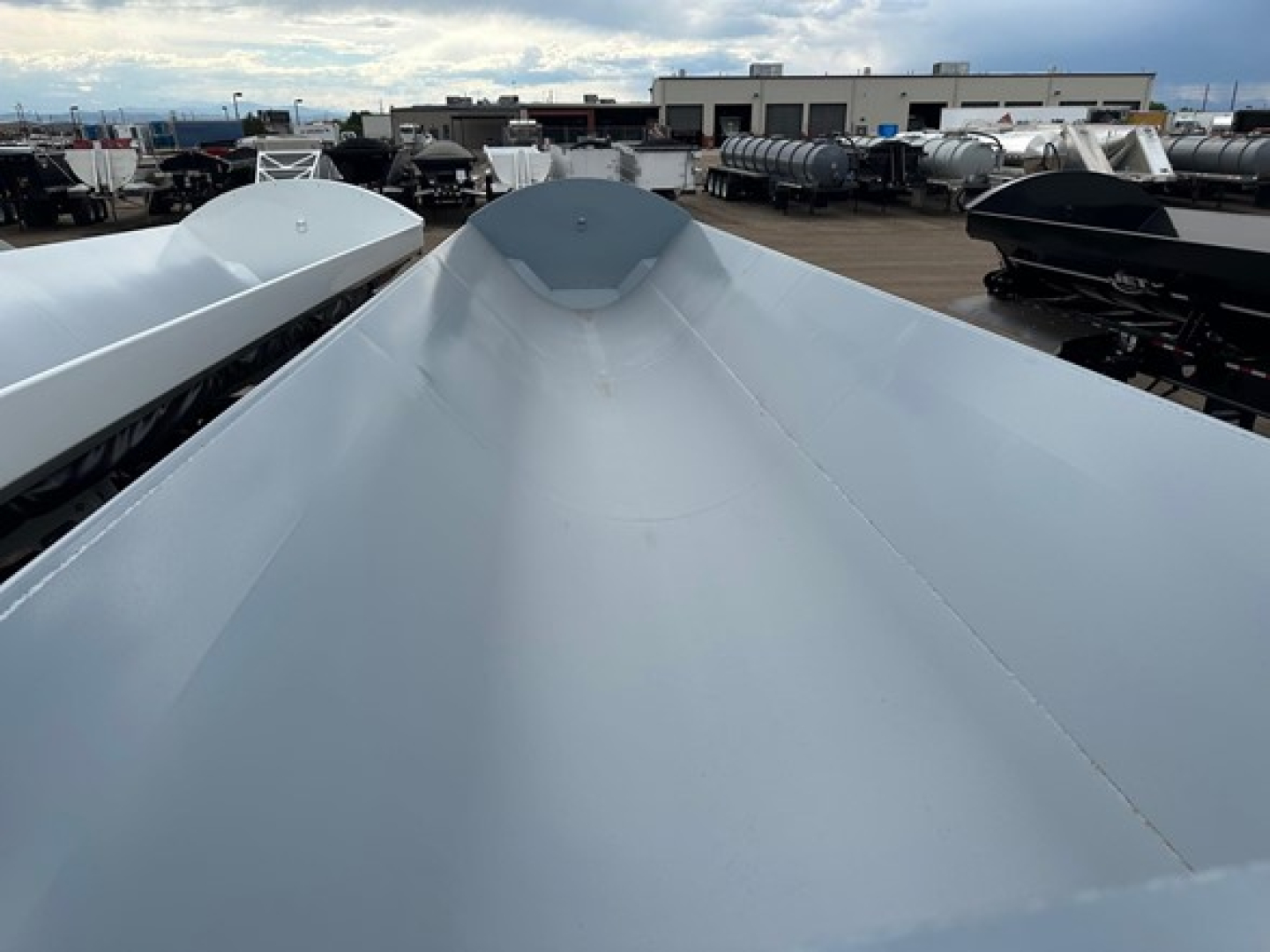 Trailer top perspective showing a central raised peak with smooth silver side panels and other trailers in the background.