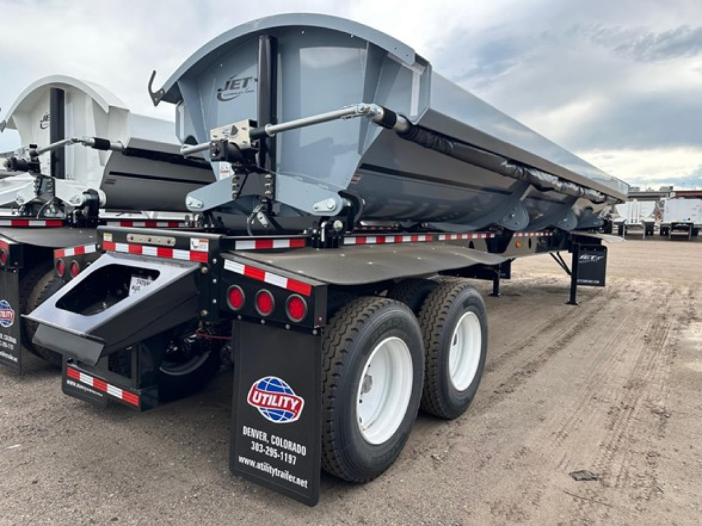 Jet Air Ride Side Dump trailer showing dual-axle rear, grey dump body, landing gear, and safety reflectors. Text on rear: utility logo, contact info; Certificate/brand details visible on bumper area.