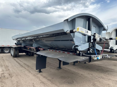 Jet air ride side-dump trailer showing curved aluminum body and hydraulic mechanisms with a landing gear and underside view.