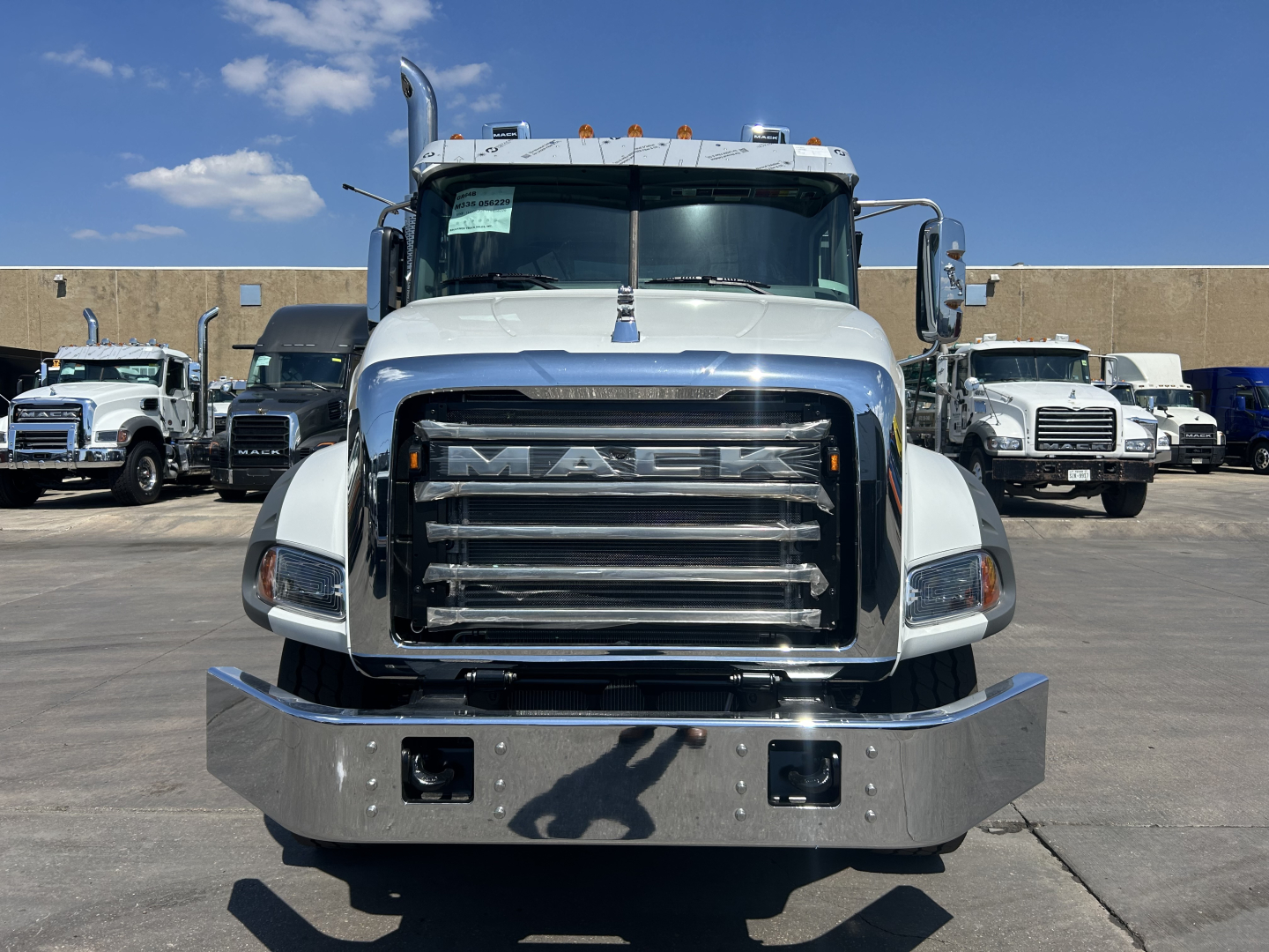 Front view of a white 2026 Mack GR64B rolloff truck showing large chrome grille with MACK emblem, bumper, and side mirrors.