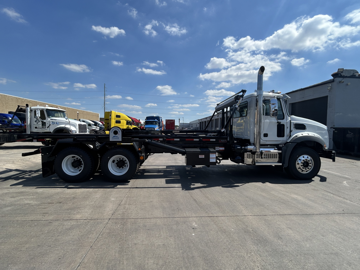 2026 Mack GR64B roll-off truck side profile showing long flatbed and crane/hoist with exhaust stack, white cab, and multi-axle configuration.