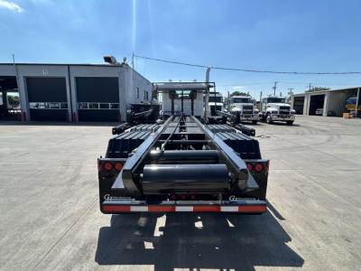 Truck chassis rear view showing roll-off container system and rear lights on a Mack GR64B chassis with flatbed rails.