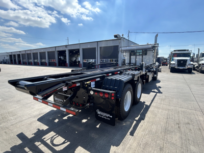 Rear view of a new 2026 Mack GR64B roll-off truck showing its long trailer hook lift apparatus and dual rear axles with white rims.