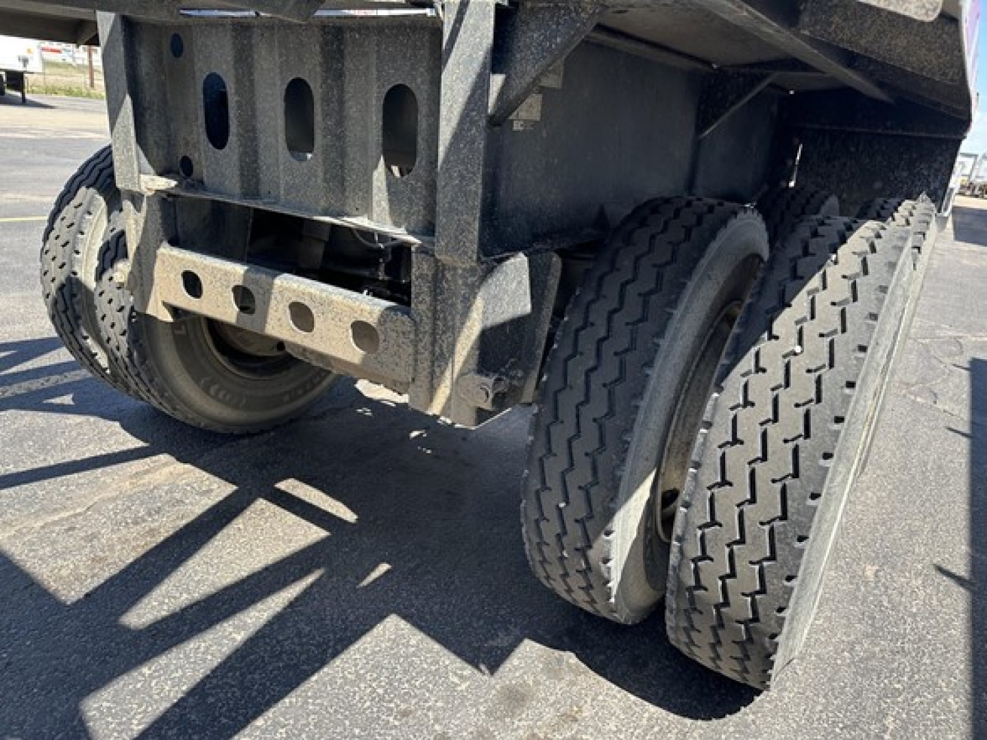 Bottom dump trailer showing dual rear wheels and chassis with metal frame and mudflaps.