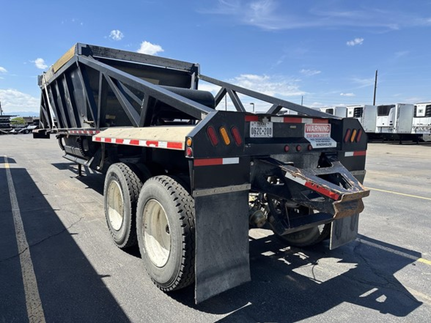 Bottom dump trailer showing rear view with dual rear tires and hydraulic dump bed, black frame with reflective tape and warning labels.