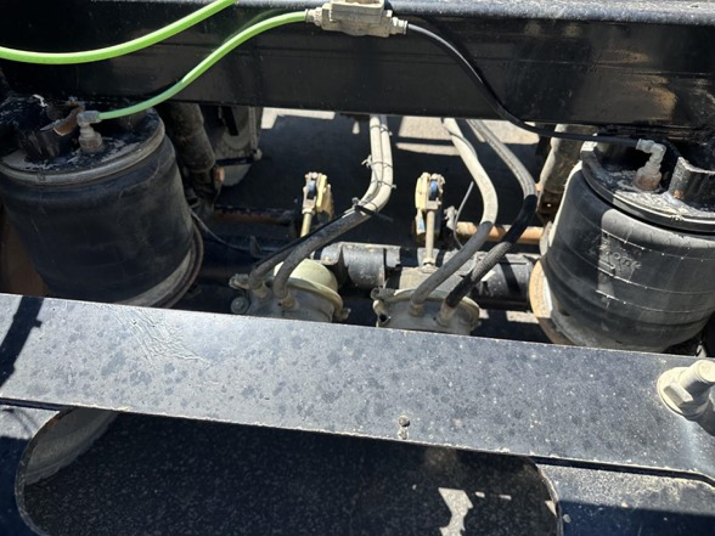 Bottom dump trailer undercarriage with air tanks, hoses, and hydraulic lines visible. Components include two cylindrical air reservoirs, metal frame, and various control lines.