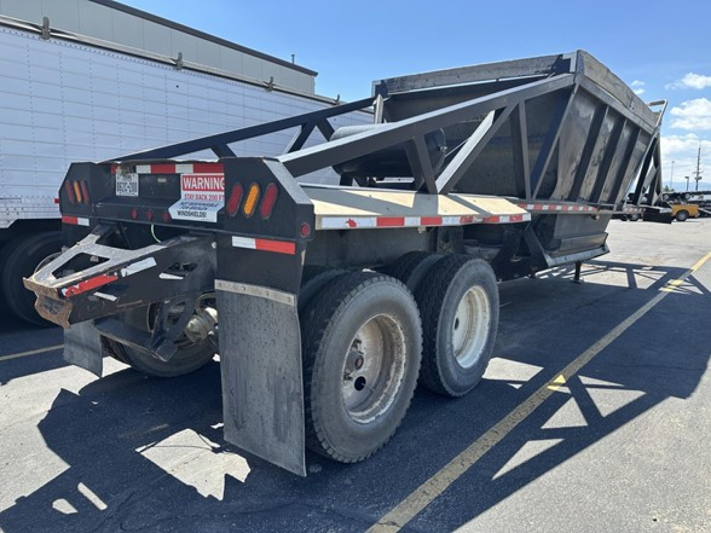 Dump trailer showing dual rear axles with a raised open-top cargo bed and warning labels on the back.