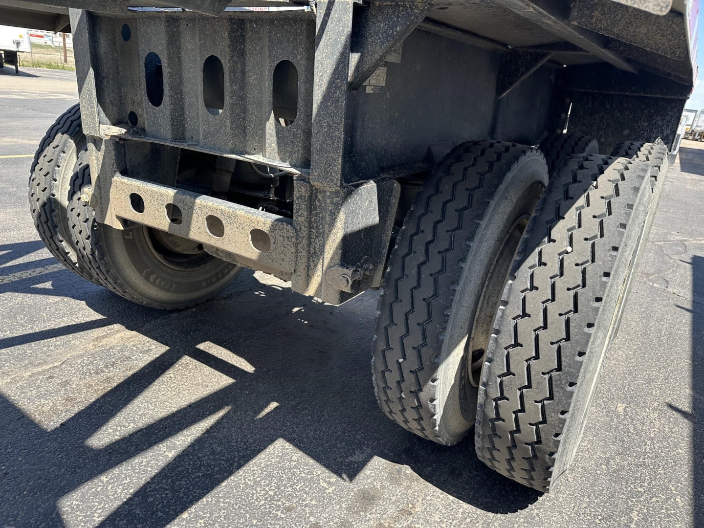 Trailer rear end showing dual rear axles and heavy-duty suspension with air ride bag and flip tarp system in a dump trailer.