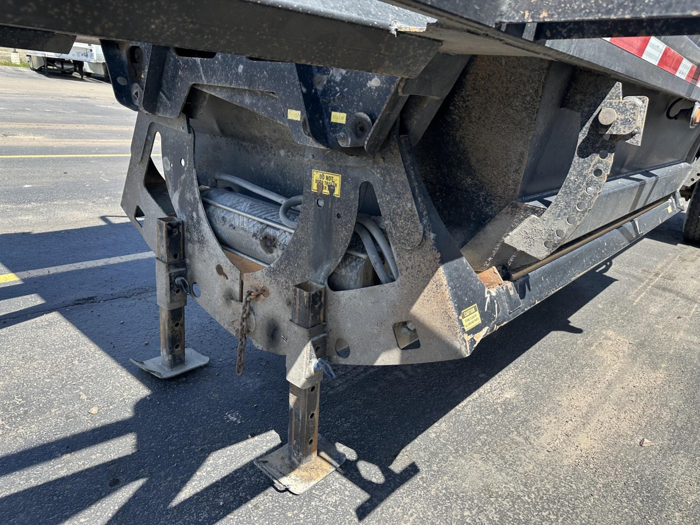 Trailer undercarriage showing hydraulic components and steel frame of a 40' air ride bottom dump with electric flip tarp. Visible are landing legs, structural brackets, and a coiled hose.