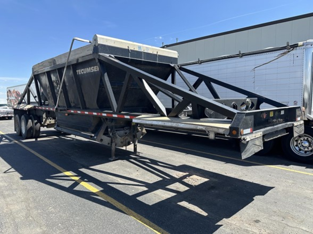 Dump trailer showing structural frame and Tecumseh hopper with reflective tape along frame and dual rear axles.