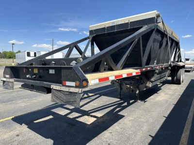 Bottom dump trailer showing side rails and rear tandem axle with reflective tape and black paint.