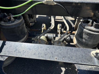Bottom dump trailer undercarriage with air tanks, hoses, and hydraulic lines visible. Components include two cylindrical air reservoirs, metal frame, and various control lines.