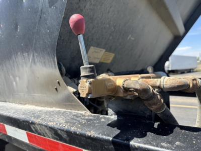 Valve lever and hydraulic line on a bottom dump trailer with black metal frame and rust-colored fittings.