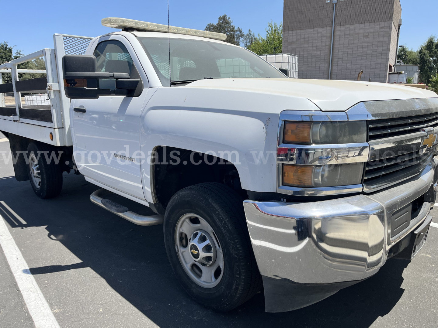 Chevrolet Silverado 2500HD flatbed dump truck in white with chrome bumper and side steps, front grille and headlight detail visible.
