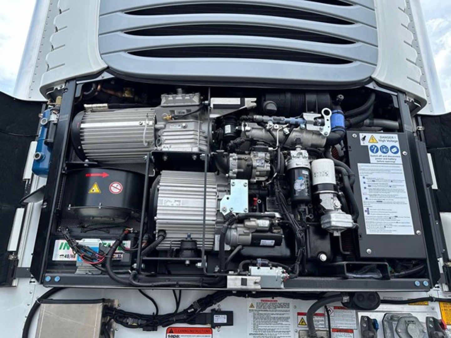 Diesel engine bay of a 2027 Utility Cargo Bull 625 trailer showing engine components, hoses, wiring, and a rider panel with safety labels.