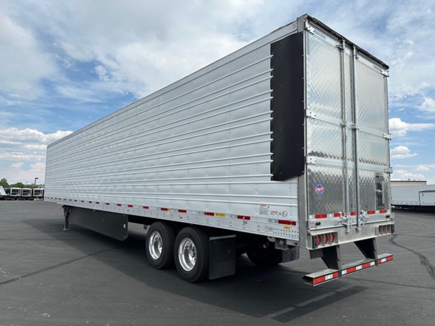 Trailer rear view showing aluminum cargo box and dual rear doors with diamond plate and reflective safety tape.