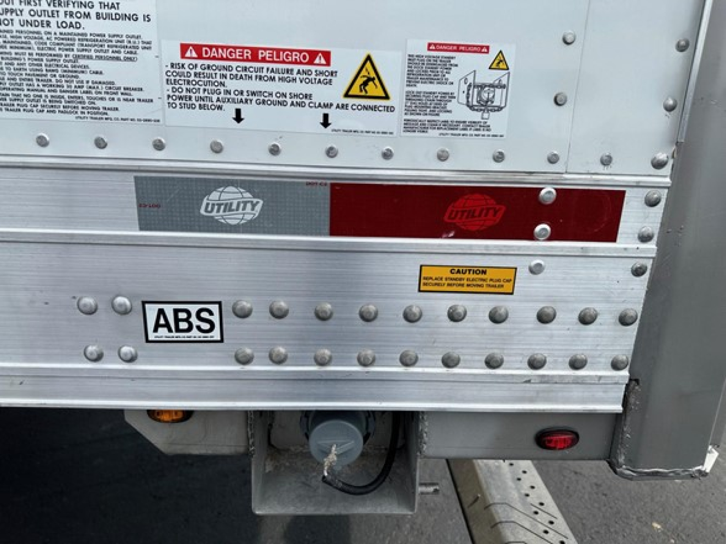 Trailer rear showing ABS sticker, Utility branding, warning labels, and a hitch/tow system with metal riveted panels.