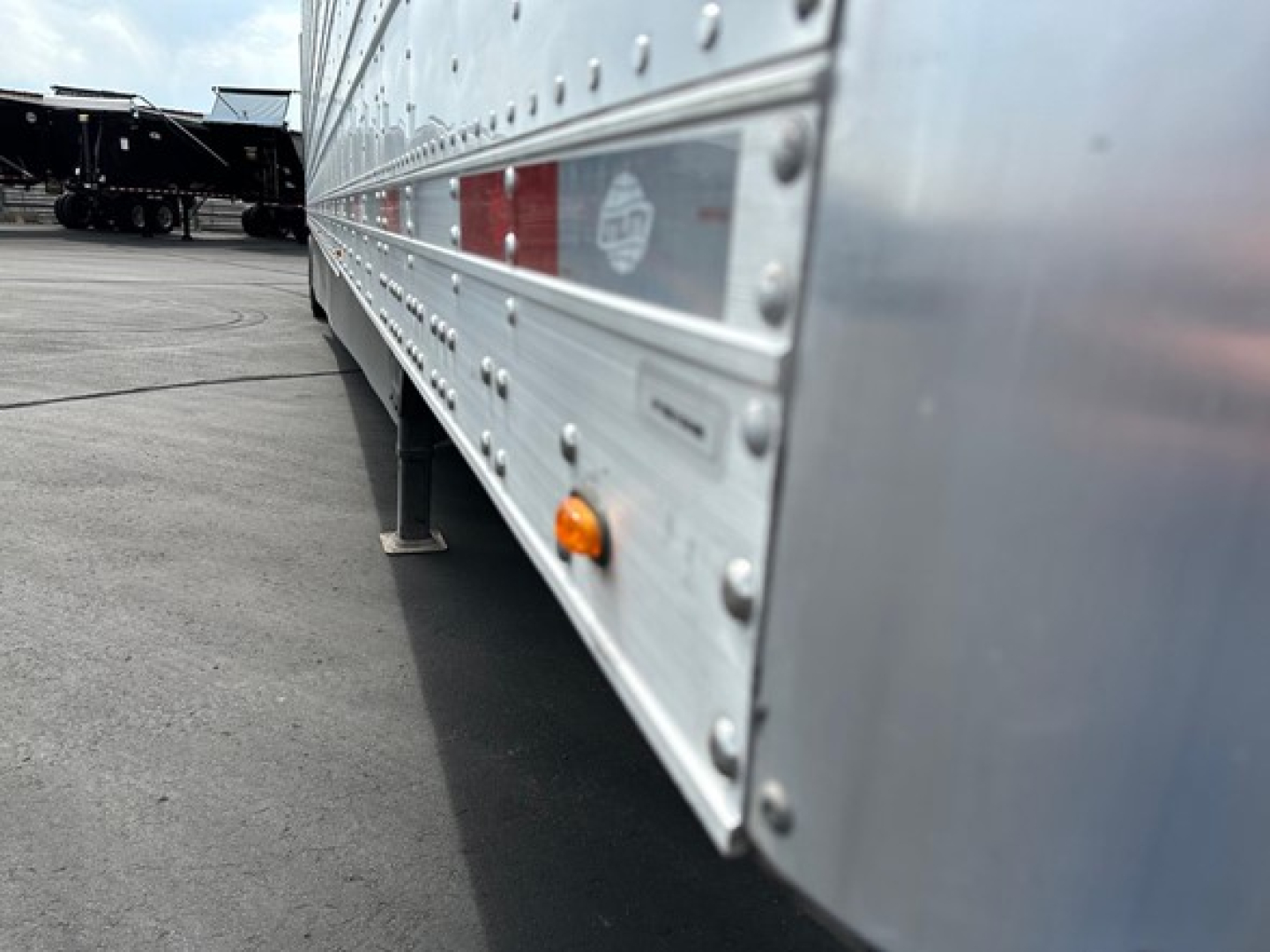 Trailer side with riveted aluminum paneling showing orange marker light and reflective strip.