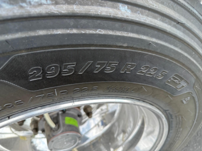 Tire sidewall showing 295/75 R22.5 marking on a trailer near a brake drum and wheel rim.