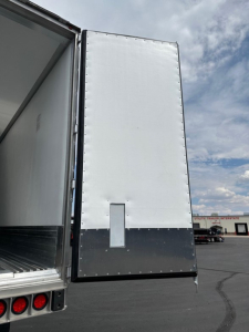 Tractor-trailer rear door of a 2027 Utility Cargo Bull 625 Hybrid reefer trailer showing ribbed white exterior with a small rectangular vent panel and edge fasteners.