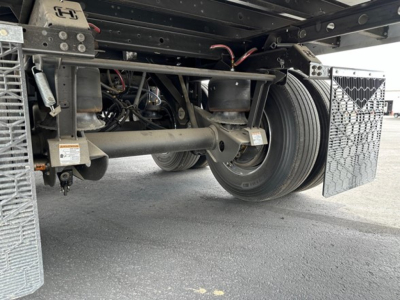 Rear-axle suspension and dual tires of a utility trailer, hydraulic lines, and metal steps visible underframe.