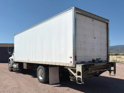 Truck rear/side view showing a white box truck cargo area and International 4400 cab in a yard.