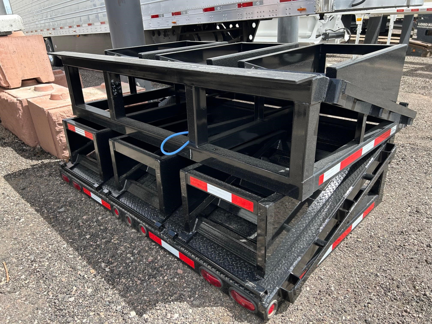 Neville Beaver Tail W 3 Flip Ramps trailer deck and frame stacked with loading ramps folded, black steel construction, reflectors and LED lights along sides.