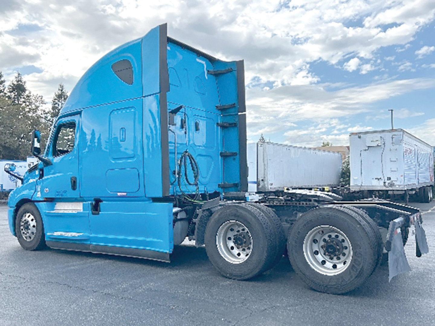Freightliner Cascadia126 sleeper tractor truck side view with blue cab and attached trailerless chassis.