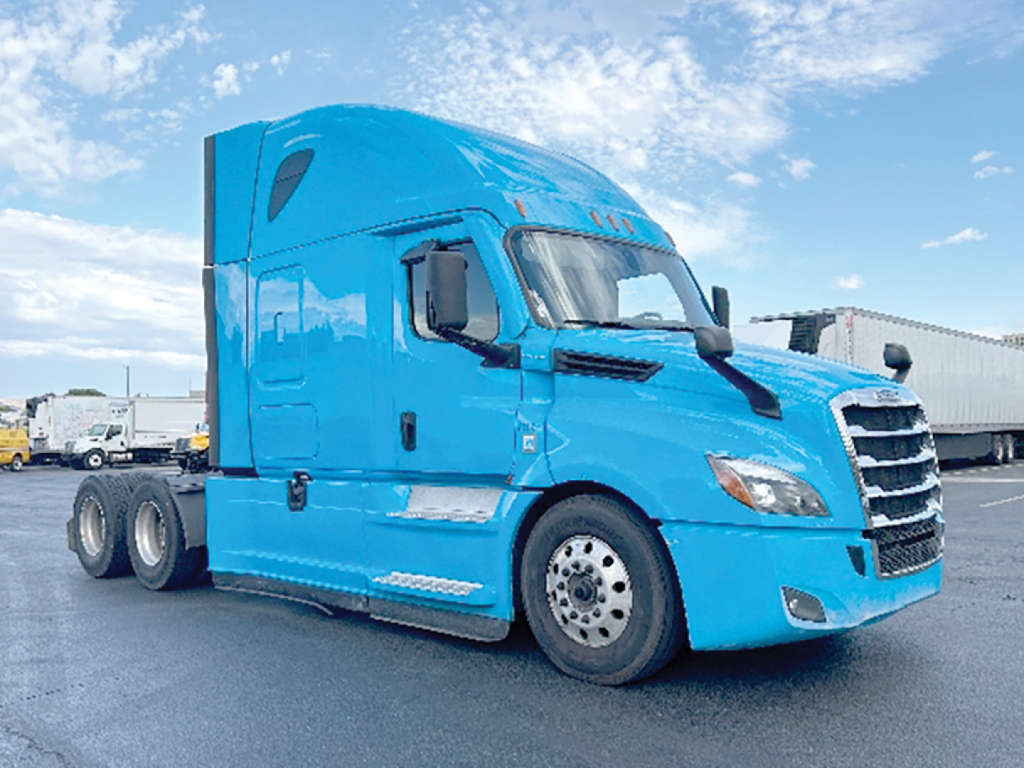 Truck cab in blue with Freightliner-like grill, side mirror, and wheels visible; no legible text on the cab or nearby in the image.