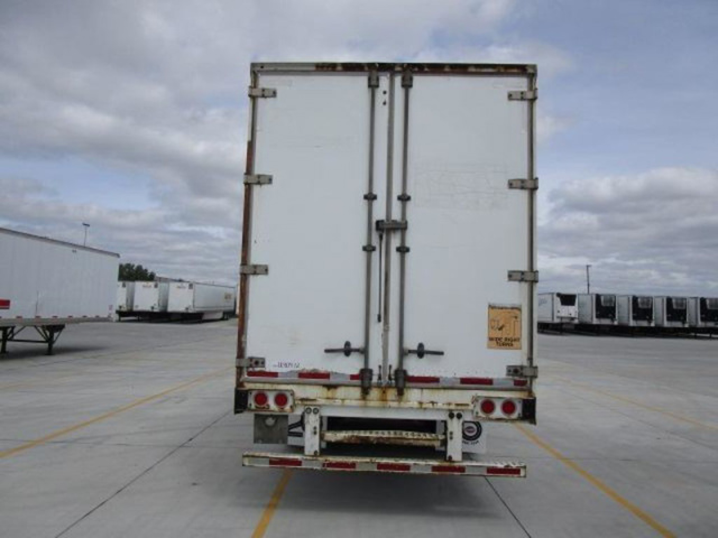 Back of a white Stoughton van trailer with double rear doors, hinges, latches, and red/white reflective markings. Small yellow caution sticker on right door. Trailer in a lot.
