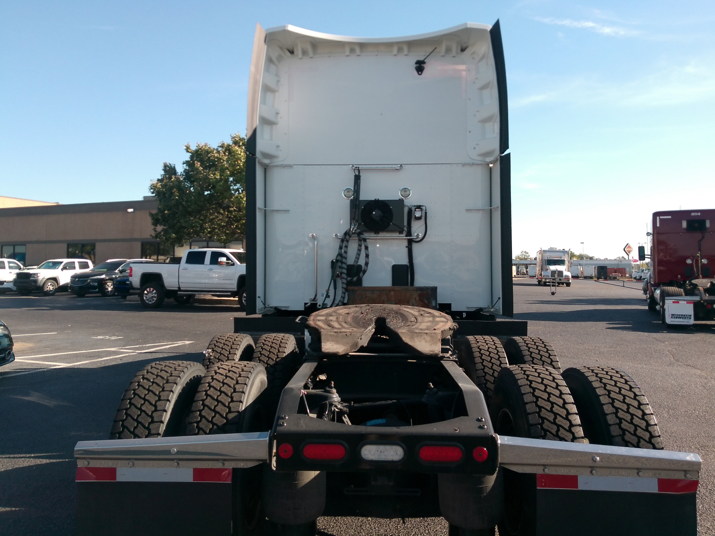 Rear view of a Peterbilt 579 truck tractor showing dual rear axles and fifth-wheel hitch with exposed driveshaft and frame, in a truck lot.