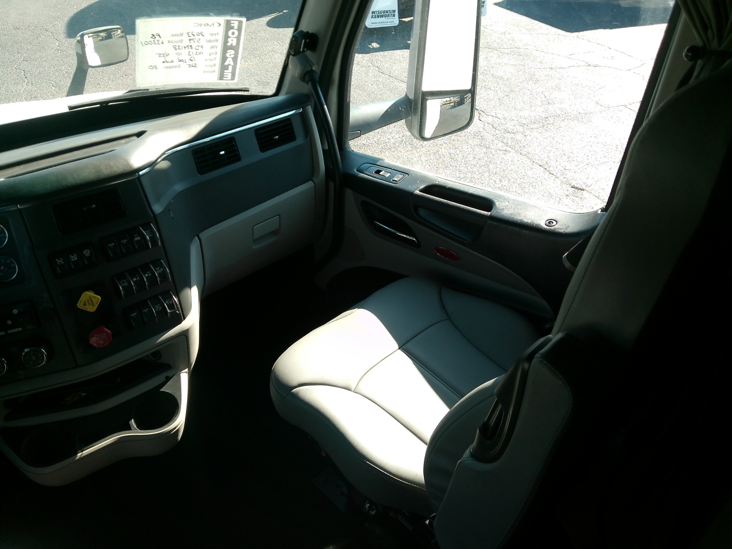 Vehicle cab interior of a Peterbilt 579 showing driver's seat, dashboard controls, and side mirror view.