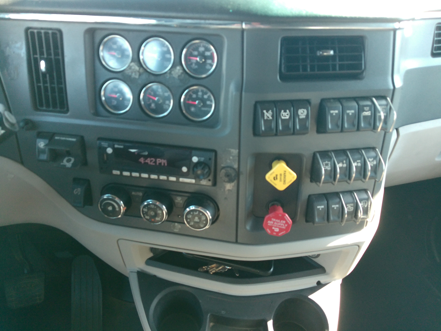 Peterbilt 579 dash panel showing multiple gauges, A/C controls, radio, switches, and 12V outlets.