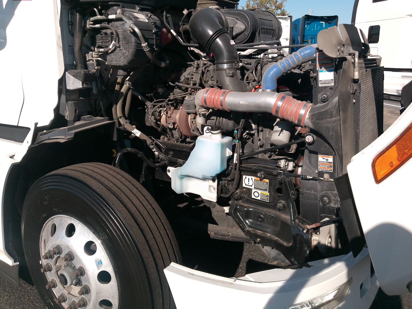 Peterbilt 579 engine bay with label text on decals and components; visible components include air intake, coolant reservoir, hoses, and engine block.