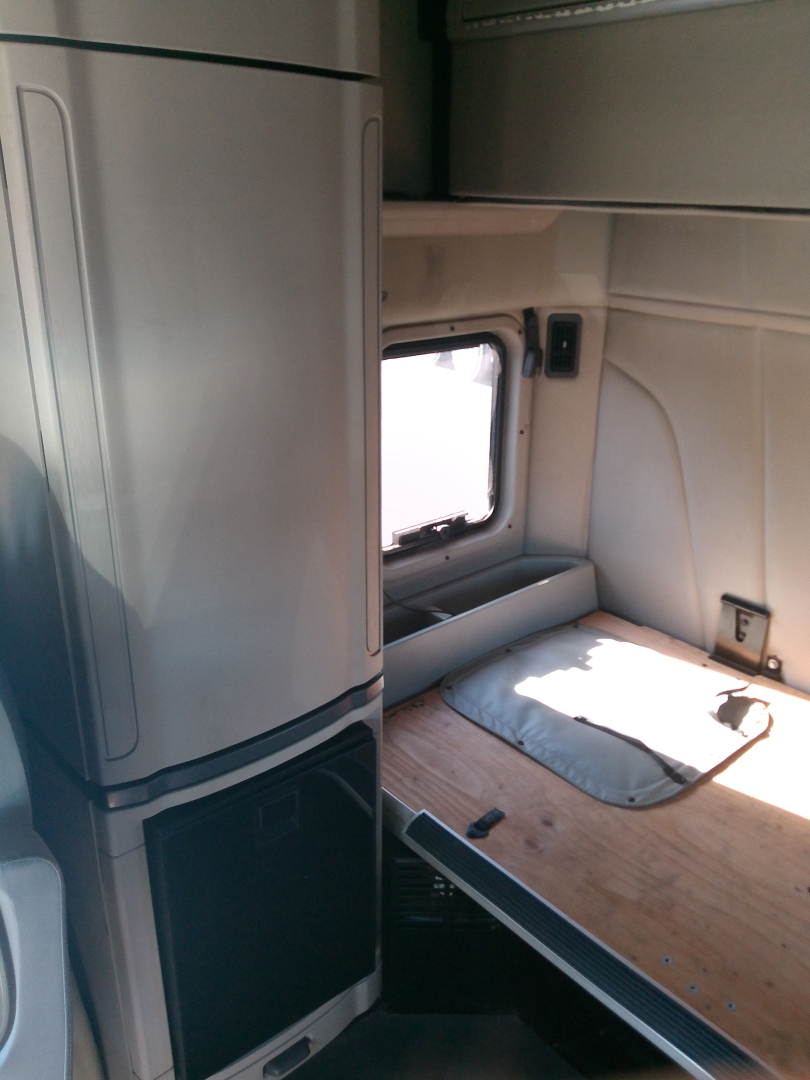Peterbilt 579 truck cab interior with sleeper area and window, bench-style bed platform, small shelf, and light wood surface.