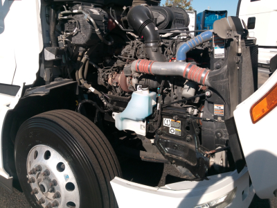 Peterbilt 579 engine bay with label text on decals and components; visible components include air intake, coolant reservoir, hoses, and engine block.