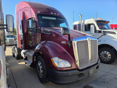 Kenworth T680 tractor-trailer cab in maroon showing front grille and number 444, side mirror, and dual rear sleepers in a truck lot.
