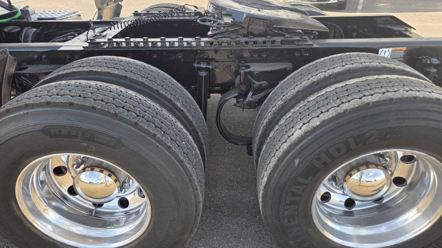 Kenworth cab rear wheels and drivetrain area with dual rear axles and chrome hubcaps; visible tires showing tread and wheel rims