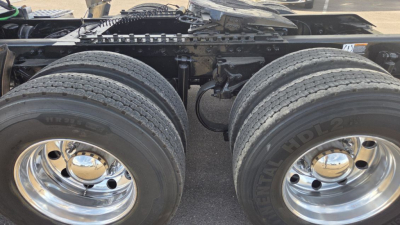 Kenworth cab rear wheels and drivetrain area with dual rear axles and chrome hubcaps; visible tires showing tread and wheel rims