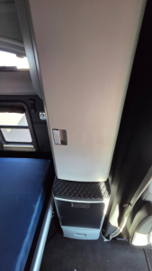 Truck interior side panel and step area of a 2022 Kenworth T680, showing a small storage drawer and metal diamond-plate step near a beige vertical panel.