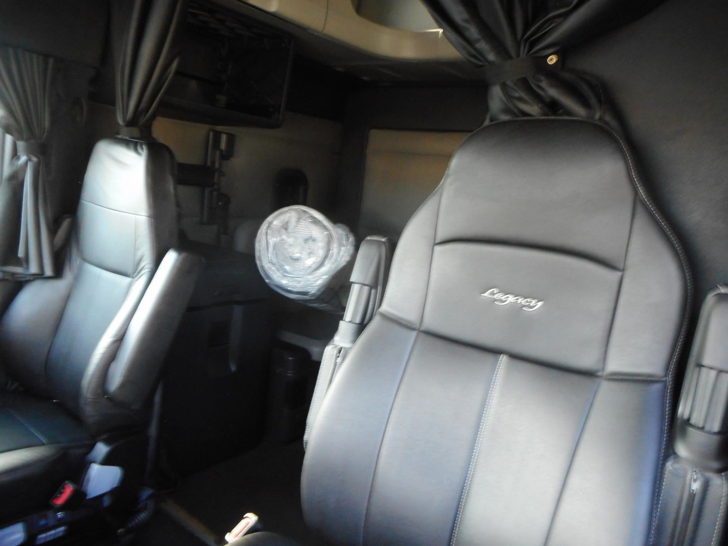 Truck interior view of a 2022 Freightliner Cascadia 126 showing driver seat with grey leather, dashboard, and overhead sleeper area.