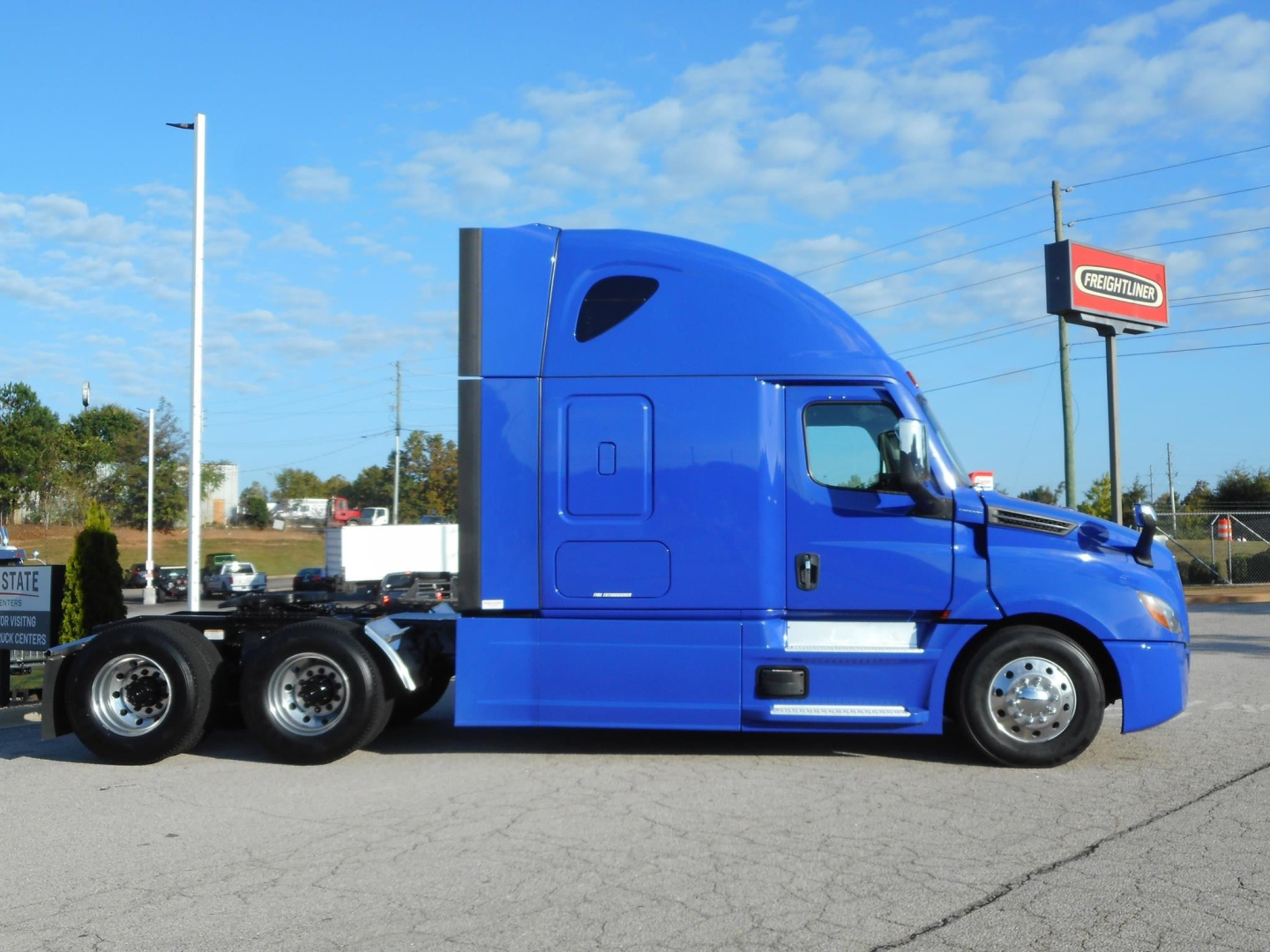 Side view of a blue Freightliner Cascadia 126 sleeper tractor with dual rear axles and chrome wheels.