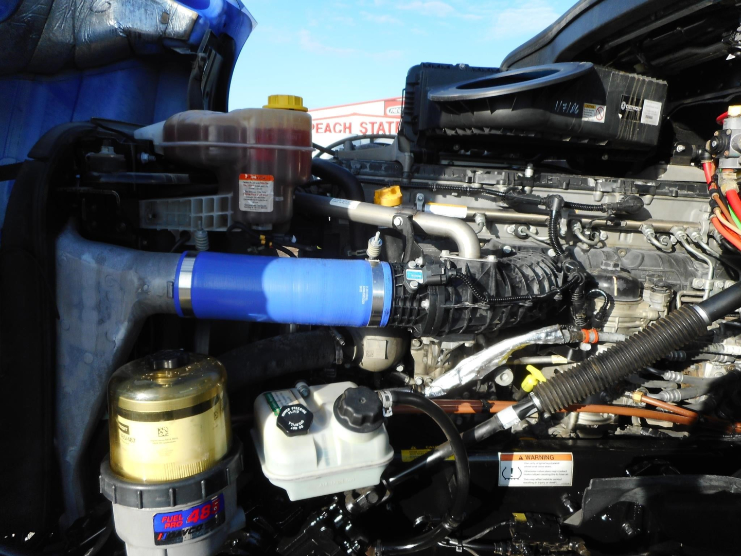 Freightliner Cascadia engine bay showing blue silicone hose, coolant reservoir, and various engine components